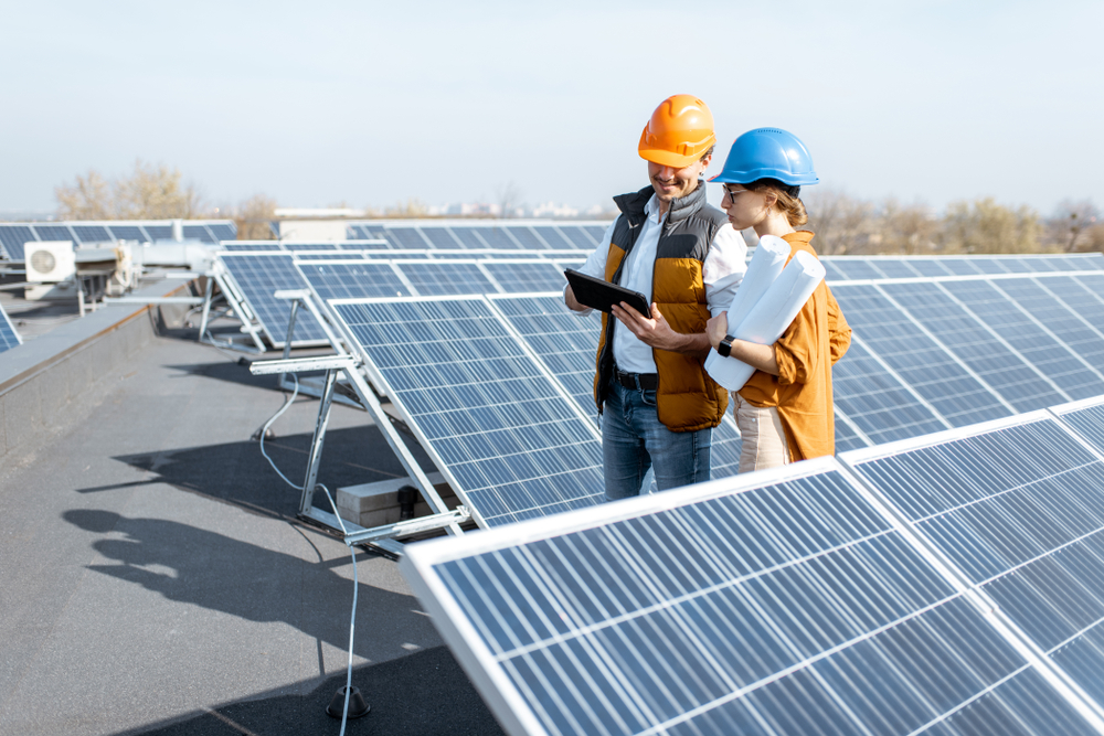 Two engineers or architects examining the construction of a solar power plant, walking with digital tablet on a rooftop